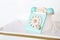 An antique blue turquoise and white rotary home phone toy made of wood rests on a white marble patterned shelf for Kidâ€™s
