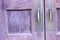 Antique brass door handles on a wooden door that has been painted purple.