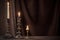 Antique candlestick with burning candle on old wooden table on background brown velvet curtain