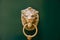 Antique door handle on a green wooden door in the shape of a lion`s face with a knock ring in the mouth.