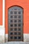 Antique door upholstered in decorative metalwork. Antique door trimmed with decorative metal elements. Orange painted