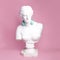 Antique female statue bust wearing blue headphones against pink background. Music lifestyle, technologies