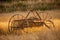 Antique hay rake in a farmers field during a golden sunset.