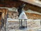 An antique outdoor lamp hanging from a bracket on a wall of an old log cabin