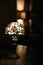 Antique table lamp with stained glass lampshade closeup on dark blurry background. Glowing mosaic lamp with floral pattern.