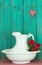 Antique water pitcher and basin with red flowers by weathered green wood background