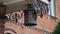 An antique wrought iron lantern hangs on the porch of the facade of an old brick building during the day and sways in the wind