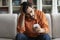 Anxious arab guy sitting on couch at home, holding smartphone