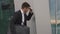 Anxious young businessman in glasses hiding from someone at the wall. Urban city background