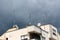 Apartment building with multiple radio and TV antennas on top mounted on strong metal poles surrounded with dark stormy blue sky