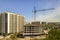 Apartment or office tall building under construction. Working builders and tower cranes on bright blue sky copy space background