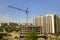 Apartment or office tall building under construction. Working builders and tower cranes on bright blue sky copy space background