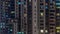 Apartment windows of a glazed skyscraper glow at night with city lights reflection aerial timelapse.