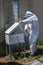 An apiarist dressed in a beekeeping suit uses a smoker to pacify the bees in a portable hive.