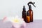 Apothecary skincare bottles and scent spray on pink background with tropical flowers bokeh, organic ingredients in skincare