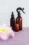 Apothecary skincare bottles and scent spray on pink background with tropical flowers bokeh, organic ingredients in skincare