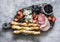 Appetizer board. Gorgonzola, ham, salami, olives, fruit, grassini on a rustic chopping board on a gray background, top view