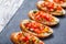 Appetizer bruschetta with chopped vegetables on ciabatta bread on stone slate background close up.
