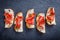 Appetizer bruschetta with jerky prosciutto on thinly sliced ciabatta bread on stone slate background close up.