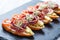 Appetizer bruschetta with prosciutto, tomato, zucchini on ciabatta bread on stone slate background close up.