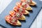 Appetizer bruschetta with prosciutto, tomato, zucchini on ciabatta bread on stone slate background close up.