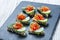 Appetizer canape with chopped vegetables and sesame on stone slate background close up