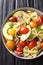 Appetizer Farfalle pasta salad with ripe avocado, onion and tomato closeup in a bowl. Vertical top view