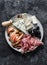 Appetizer plate - prosciutto, gorgonzola, brie cheese, olives, apples, nuts almonds on a dark background, top view