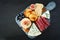 Appetizer platter with assorted cheeses and meats, overhead view on a dark stone background