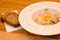 Appetizing carbonara pasta with egg yolk on a white plate in a restaurant, two pieces of bread lie on wooden table