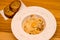 Appetizing carbonara pasta with egg yolk on a white plate in a restaurant, two pieces of bread lie on wooden table