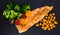 Appetizing cooked trout, chickpeas, broccoli on a black warm stone plate