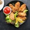 Appetizing crispy chicken wings breaded with bread crumbs with lettuce, sauce, lemon, microgreens in a plate on the