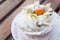 Appetizing dessert Pavlova decorated with almonds and physalis on the wooden table. Served on a saucer