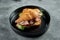 Appetizing French croissant sandwich with roast beef, tomatoes, spinach and white sauce, served in a black plate on a gray