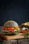 Appetizing hamburger with fresh vegetables tomato, spicy carrots, ham and parsley on a cutting wooden board and chips. A dark
