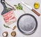 Appetizing pieces of raw bacon in a frying pan with oil, stabbed, herbs, salt and spices wooden rustic background top view clos