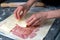 Appetizing shot of a pair of hands putting a slice of cheese on top of hams on a dough