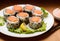 Appetizing sushi rolls with rice and salmon served on plate with green salad leaves and sesame seeds placed near chopsticks