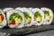 Appetizing vegan sushi roll futomaki with pepper cucumber and avocado salad on a black stone plate
