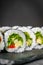 Appetizing vegan sushi roll futomaki with pepper cucumber and avocado salad on a black stone plate