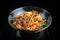 Appetizing wok udon noodles with beef, bell pepper, asparagus, sesame seeds in a black bowl on a black background with reflection