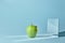 The apple is green, a square mirror on a blue background, a reflection of an apple and from shadows in a mirror.