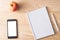 Apple, phone and notebook on a wooden background