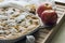 Apple pie on a white plate and two apples, wood background.