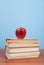 Apple on a pile of books on a wooden table and background is blue and free space for text