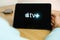 Apple TV logo on the screen of the IPad tablet with charging smart phone on the wireless charger on the wooden table