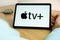 Apple TV logo on the screen of the IPad tablet with charging smart phone on the wireless charger on the wooden table