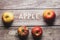 Apple written in wooden letters surrounded by red apples fruit on a wooden board