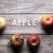Apple written in wooden letters surrounded by red apples fruit on a wooden board